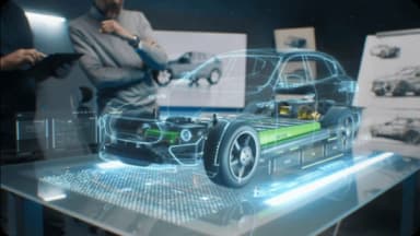 Engineers examine a holographic projection of an electric car chassis with its internal components.