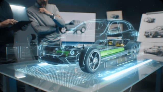 Engineers examine a holographic projection of an electric car chassis with its internal components.